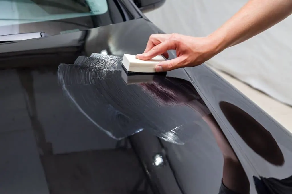 Hand applicator working a protective product across a dark car hood